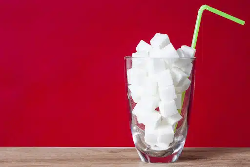 Glass with straw full of sugar and sugar cubes on red background