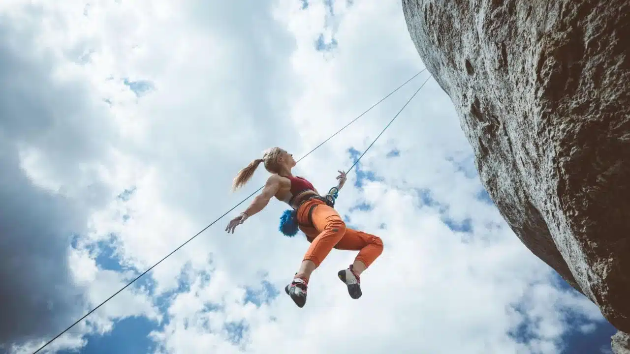 Young woman hanging on rope while climbing