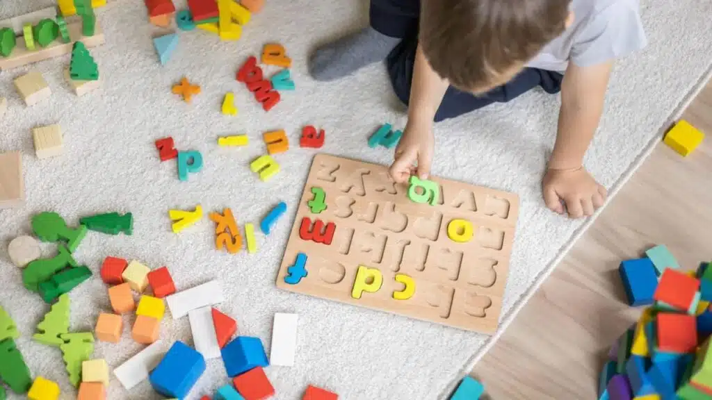 Male kid playing with wooden eco friendly alphabet letters board on table top view intellectual game