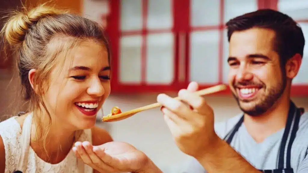 I love being his taster in the kitchen. a young man feeding his girlfriend food that he has made at home.
