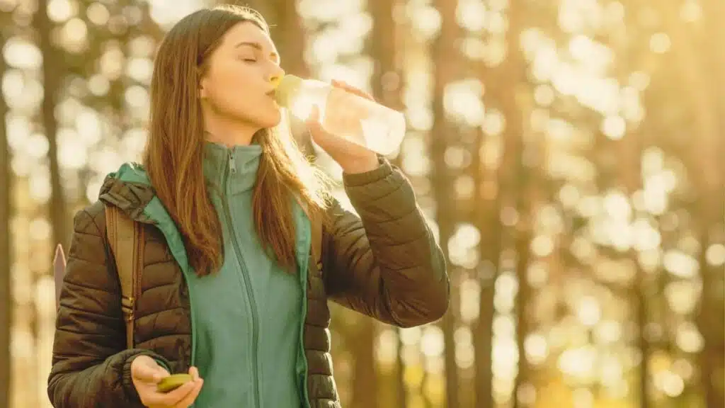 Thirsty girl drinking water while hiking by forest