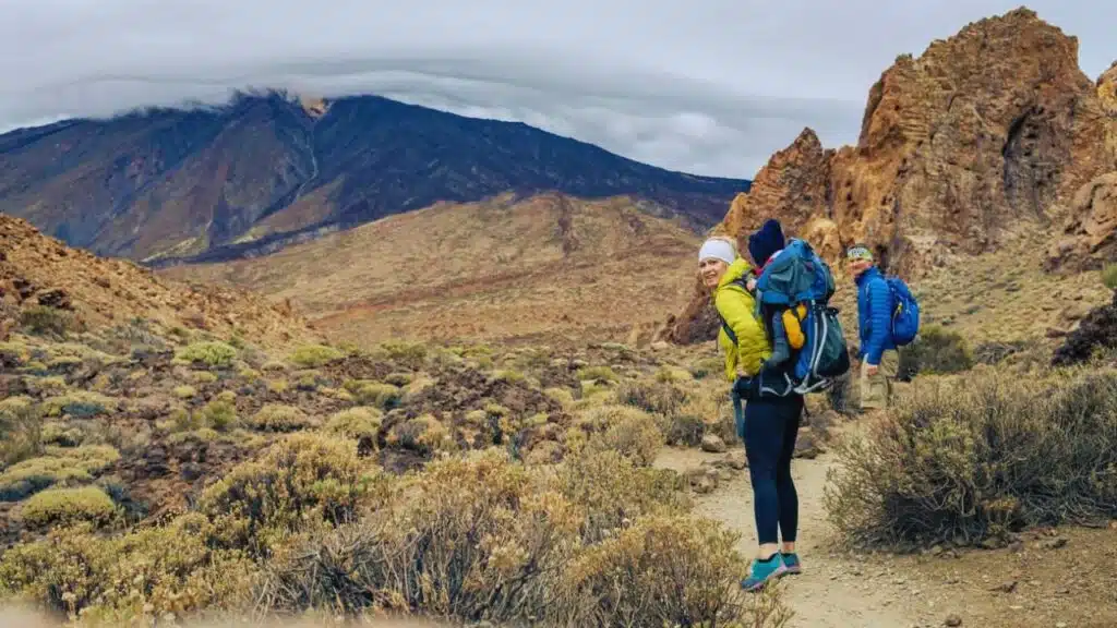 Couple hiking with baby boy travelling in backpack. Hiking adventure with child on autumn family trip in mountains