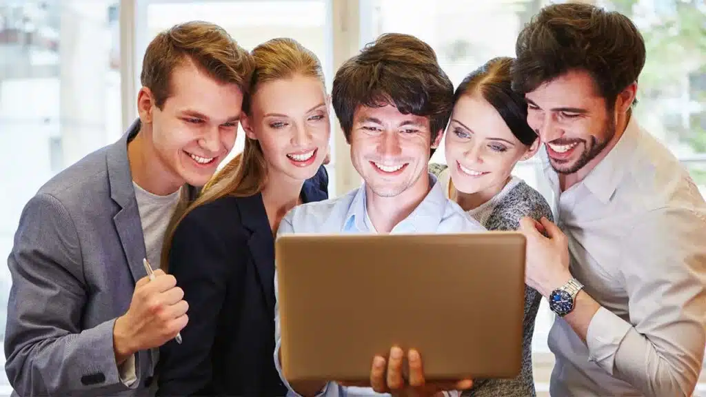 Group of colleagues smiling at a laptop, showcasing teamwork.