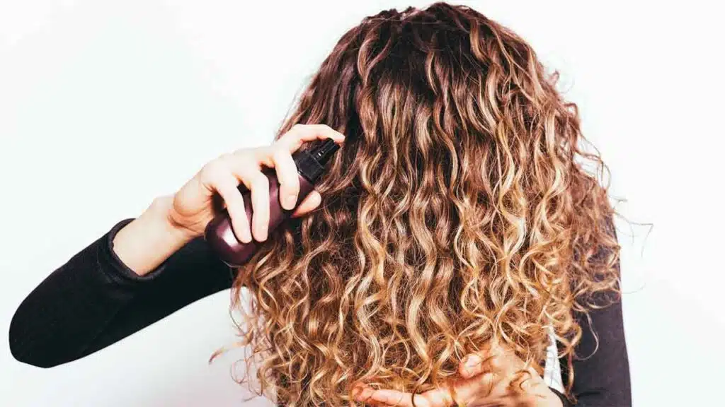 Person spraying product on curly hair.