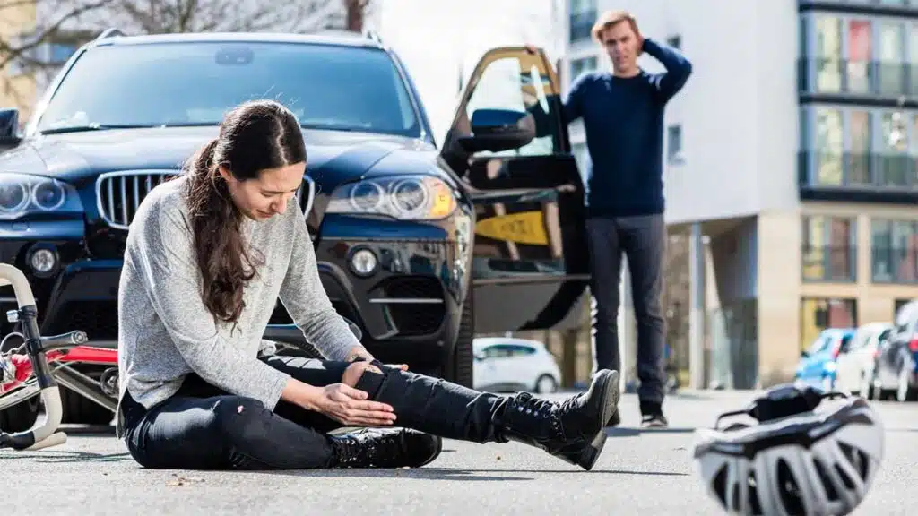 Injured woman after a bike accident with a concerned driver nearby.
