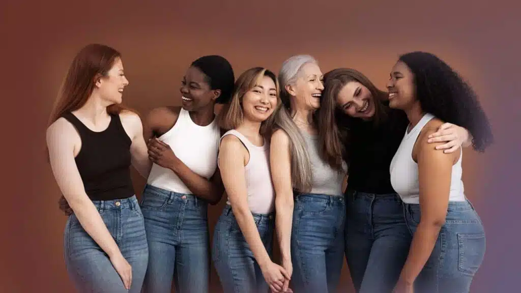 Group of diverse women smiling and embracing each other against a warm-toned background.