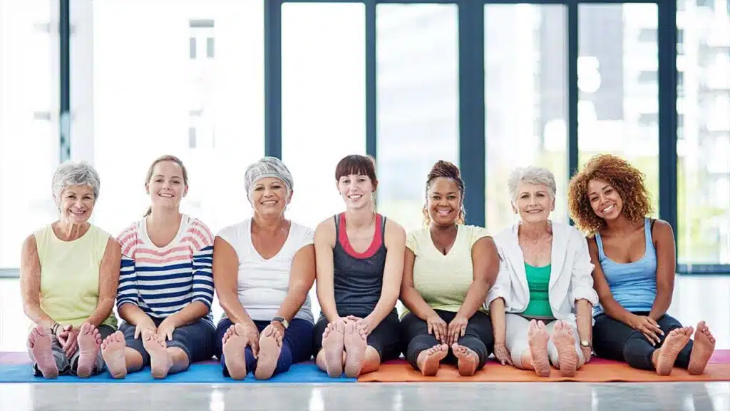 Group of women smiling while sitting on yoga mats in a studio.