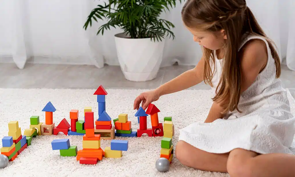 Girl playing with colorful building blocks on a carpet.