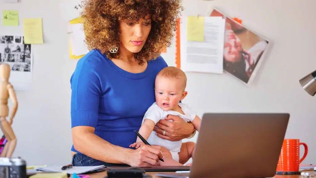 Working mom balancing baby while using laptop at home