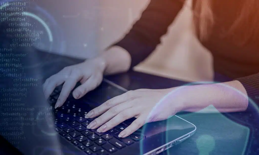 Hands typing on a laptop with cybersecurity symbols and code.