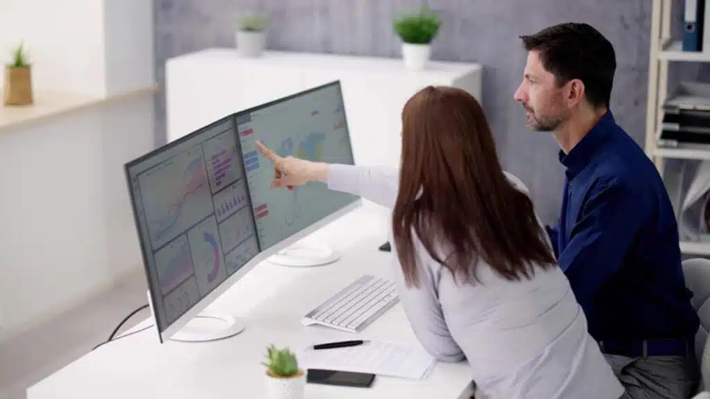 Two colleagues analyzing data on dual monitors in a modern office.