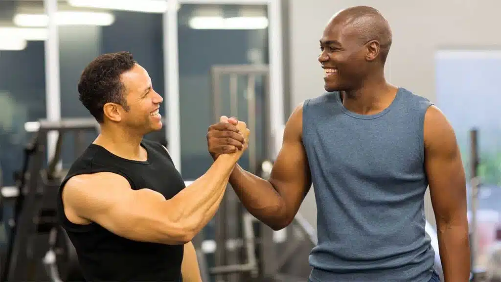 Two men in a gym, smiling and shaking hands