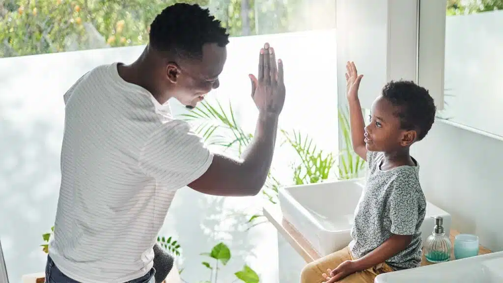 Father and son sharing a high-five in a bright room.