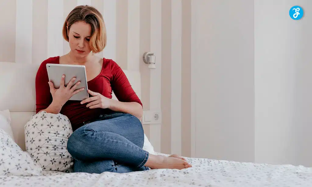 Woman sitting on a bed using a tablet in a cozy bedroom