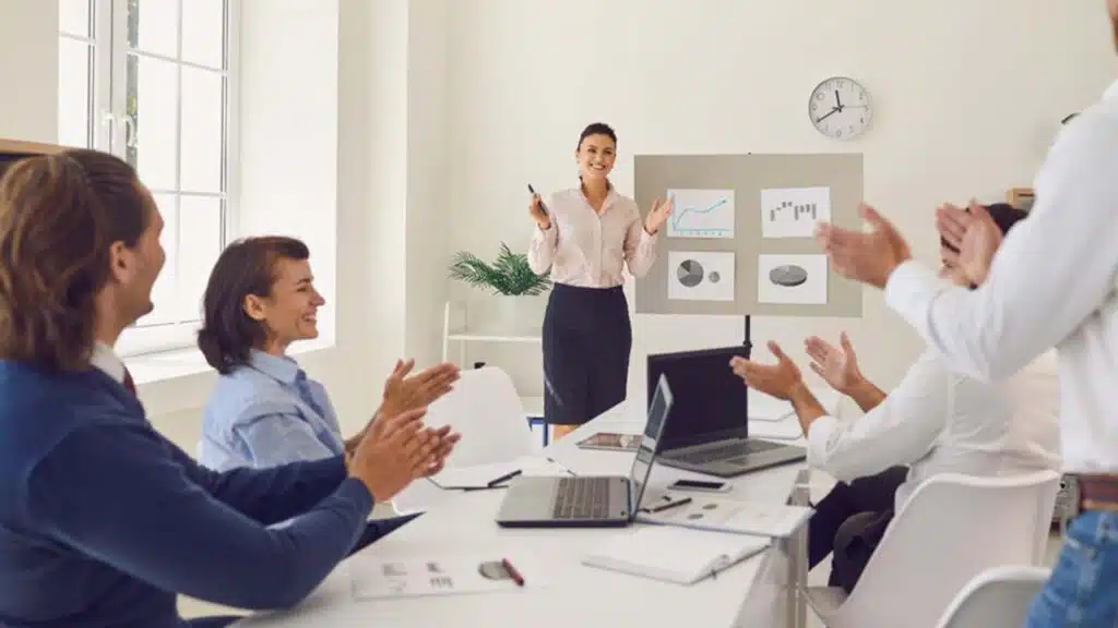 Team applauding a woman presenting graphs during a meeting in a bright office.