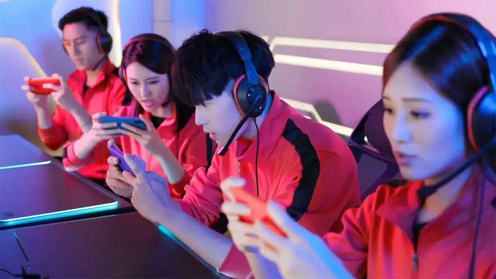 Team of gamers in red jackets playing on mobile devices with headsets on