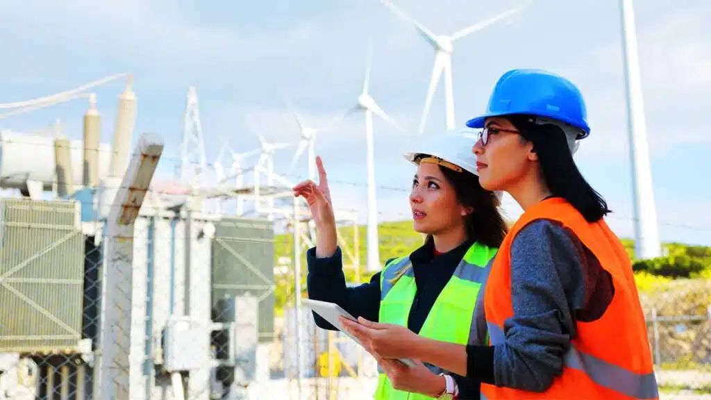 Two engineers in safety gear inspecting a wind farm with turbines in the background