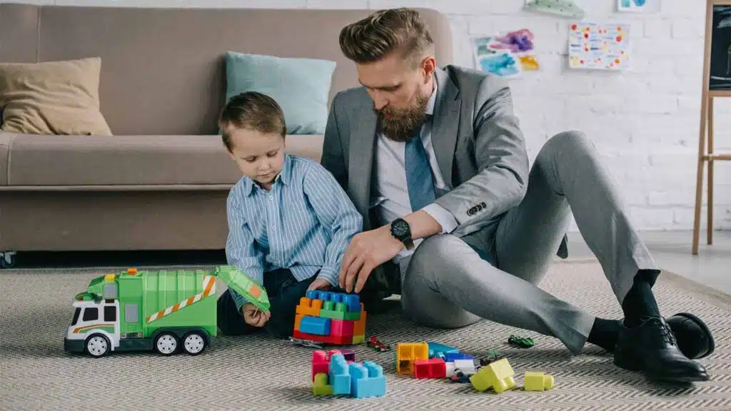 Father in business suit playing with son and toys at home