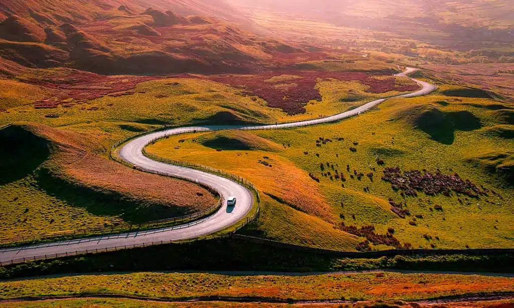 Car on a winding road through rolling green hills.