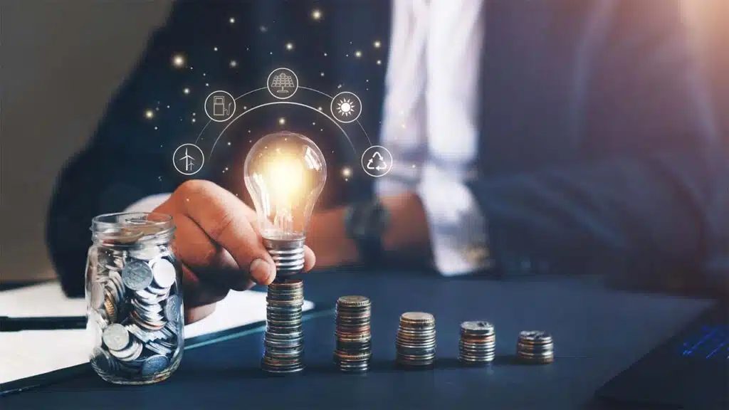 Businessman holding a glowing lightbulb above stacked coins, symbolizing investment in innovation.