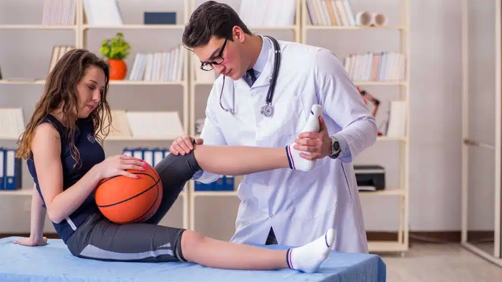 Doctor examining a basketball player's injured knee in a medical office.