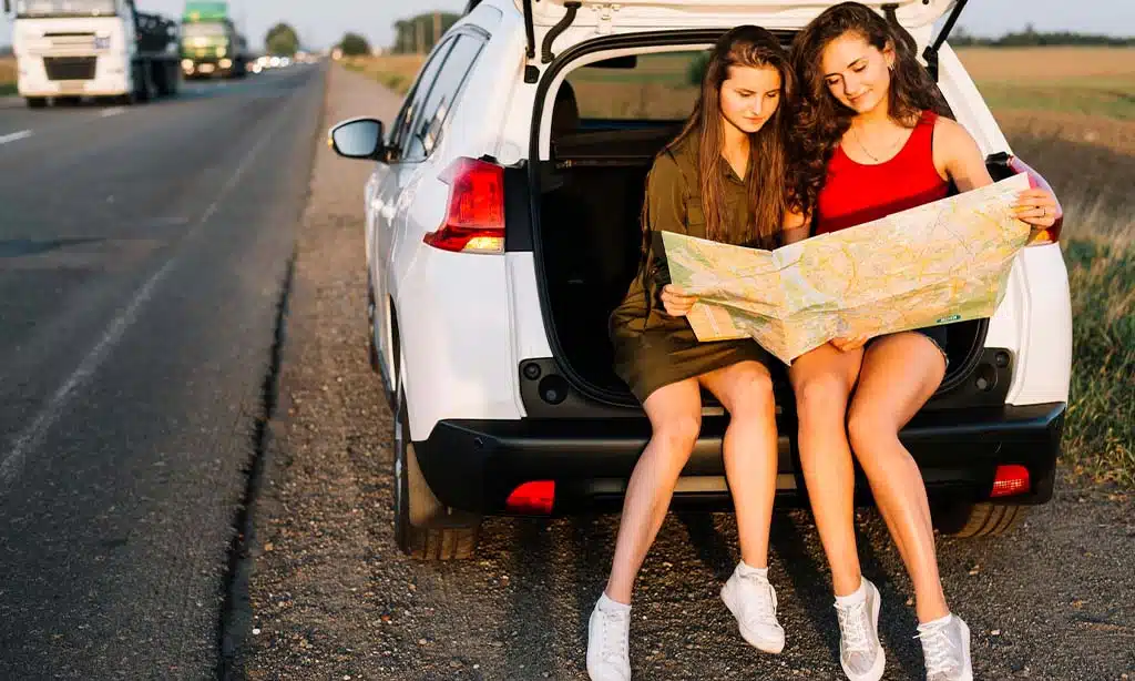 Two women in a car trunk reading a map by the roadside.