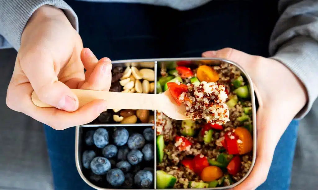 Person eating a healthy quinoa salad with fruits and nuts.