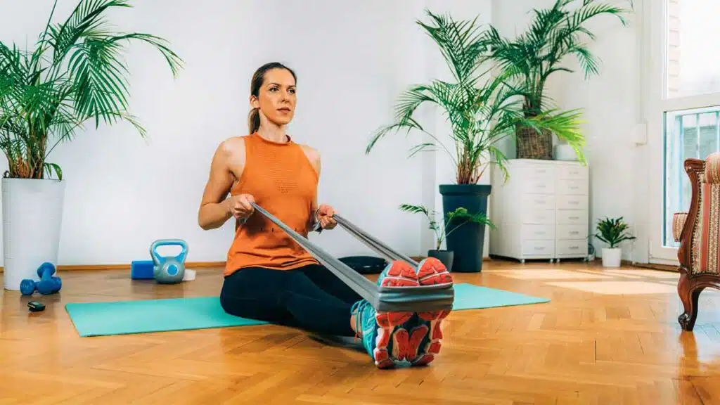 Woman doing seated resistance band row exercise at home.