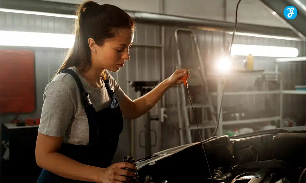 Female mechanic checking car engine oil level in a garage.