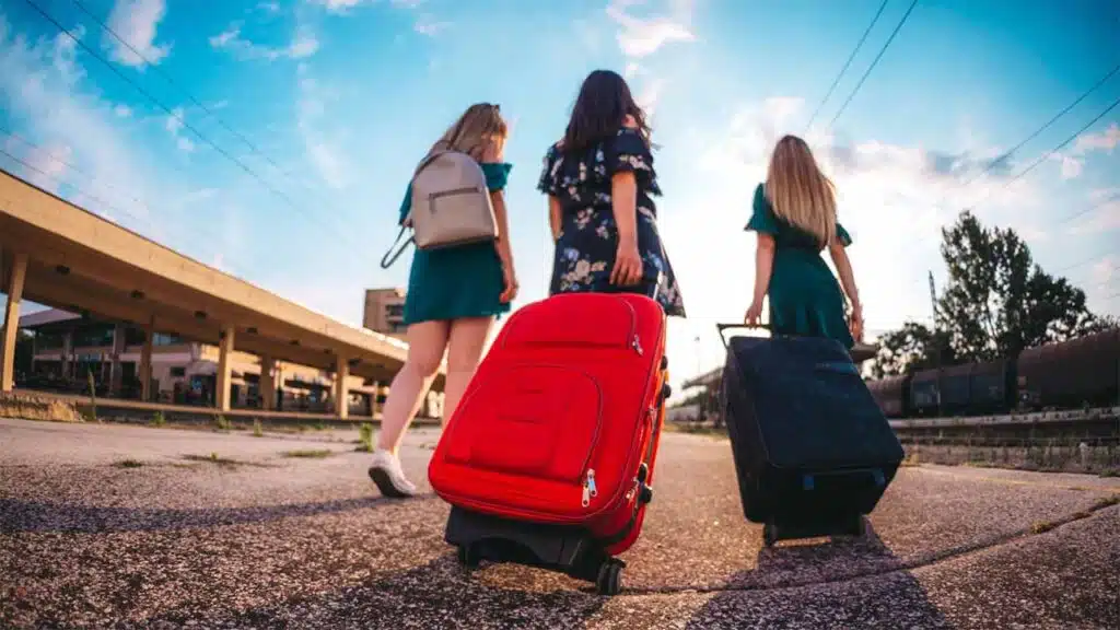 Three women with luggage walk toward a train station for vacation.