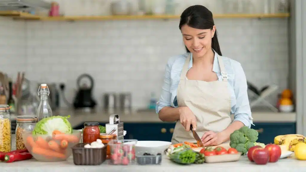 Smiling woman in an apron chopping vegetables in a bright kitchen