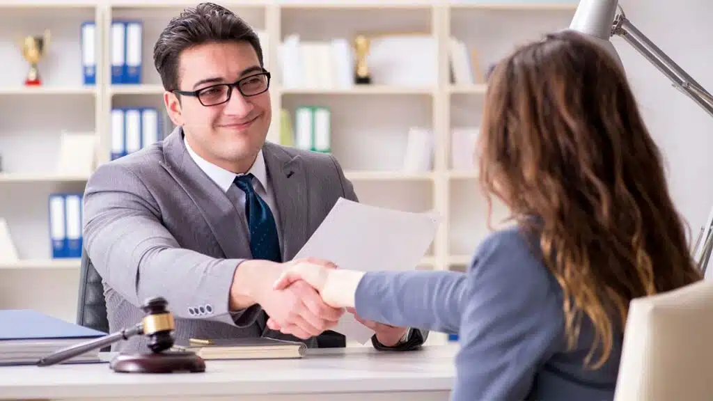 A businessman in a grey suit shakes hands with a client, sealing a deal in a professional office setting