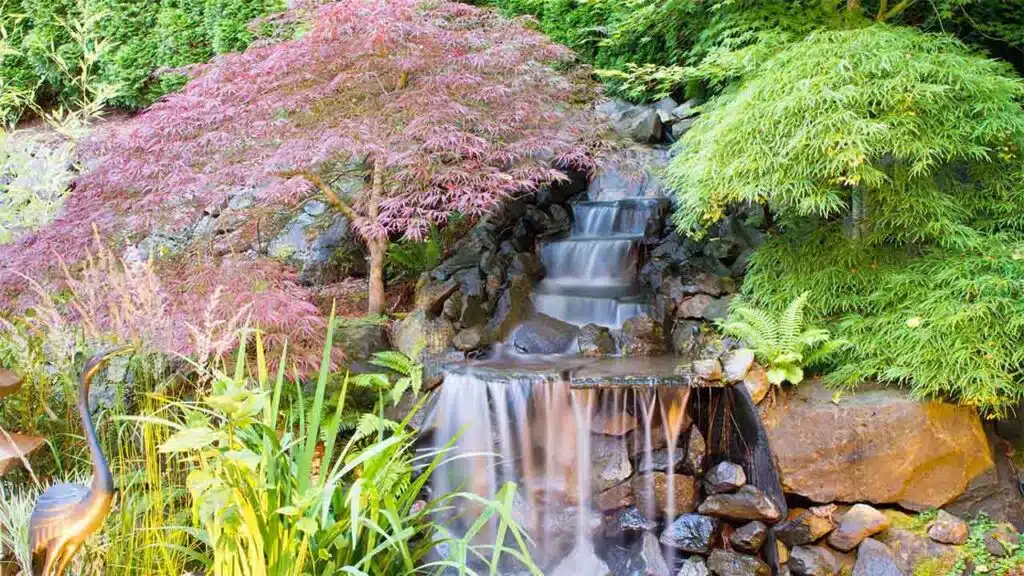 A tranquil garden waterfall cascades over dark rocks