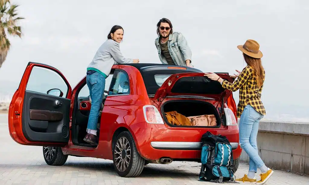 friends preparing for a road trip beside a small red car