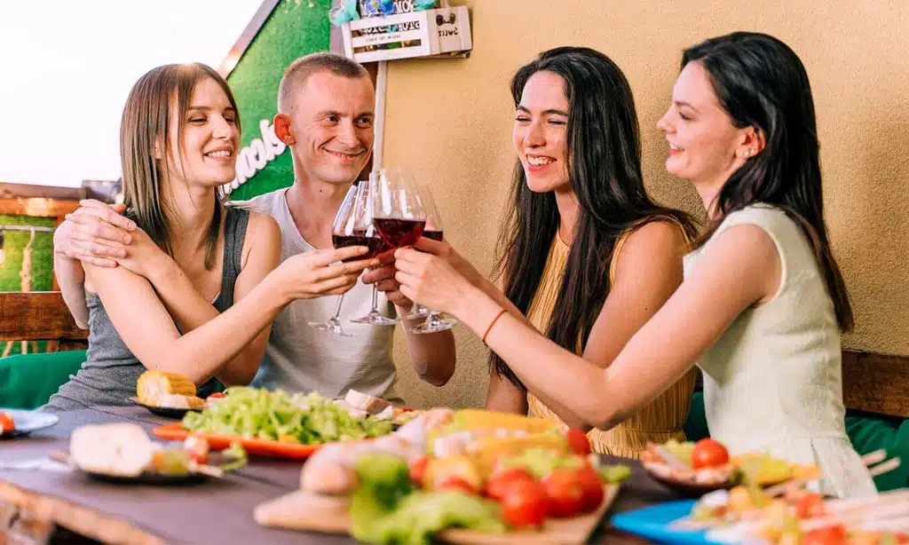A joyful group of four friends gathered around a table, clinking glasses of red wine in celebration