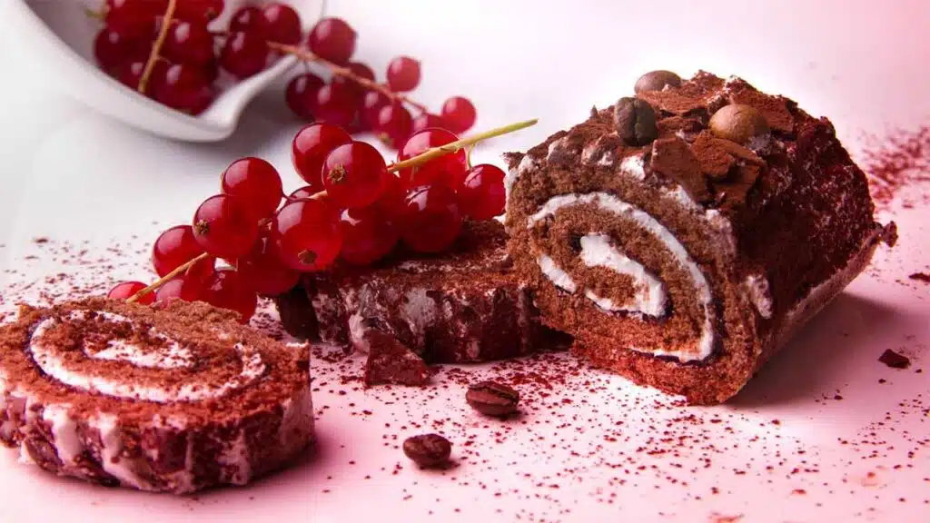 Delicious chocolate roll cake with a swirl of cream filling, garnished with cocoa powder and chocolate shavings