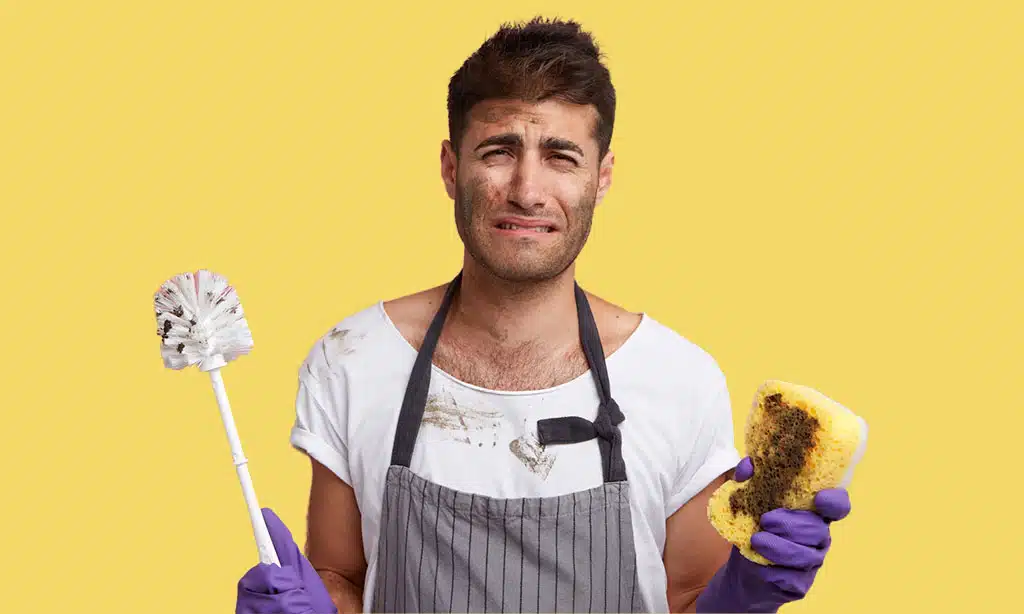 Frustrated man cleaning with dirty tools, wearing messy apron. Stressed out by tough cleaning tasks.