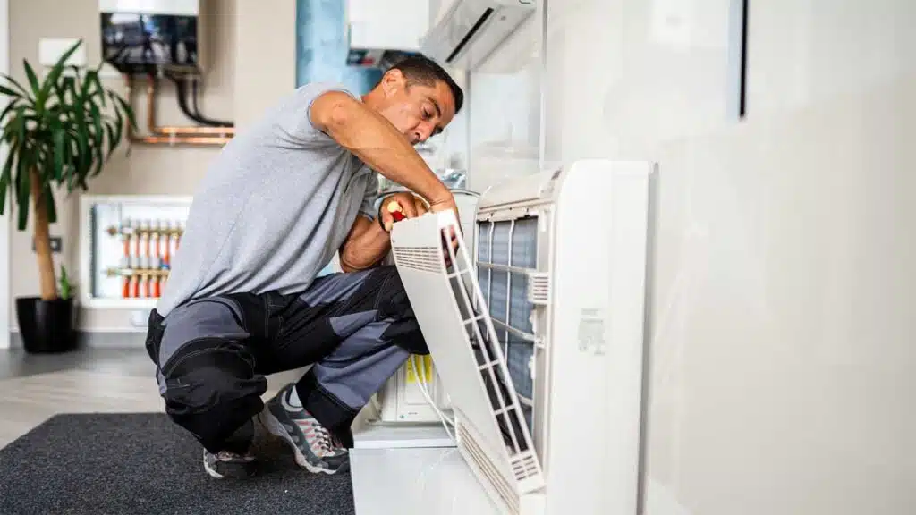 Technician repairing a wall-mounted air conditioning unit in a modern interior space.