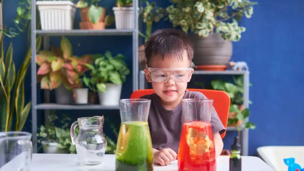 A young boy wearing safety goggles, sitting at a table engaged in a science experiment