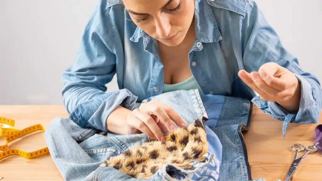 Young woman repairing denim with a leopard-print fabric patch, focusing on DIY fashion