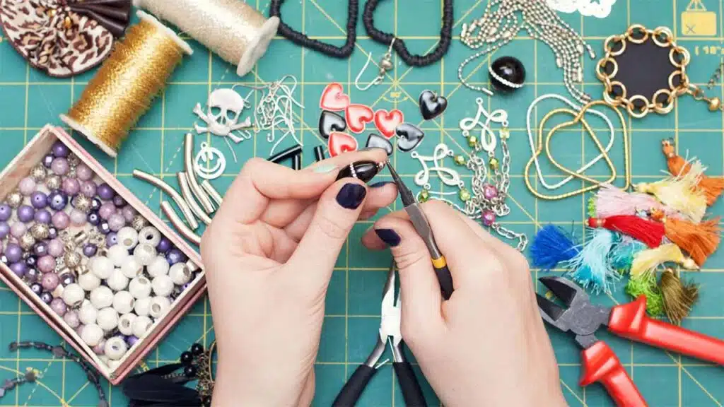 Hands working on a handmade jewelry project using pliers and a variety of colorful beads and charms