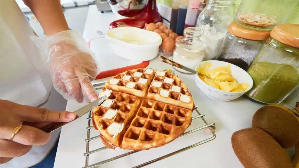 Spreading butter on freshly made waffles in a kitchen filled with ingredients