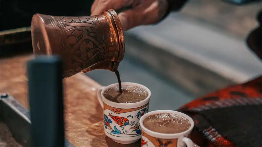 Freshly brewed traditional Turkish coffee being poured from a copper pot into beautifully patterned cups