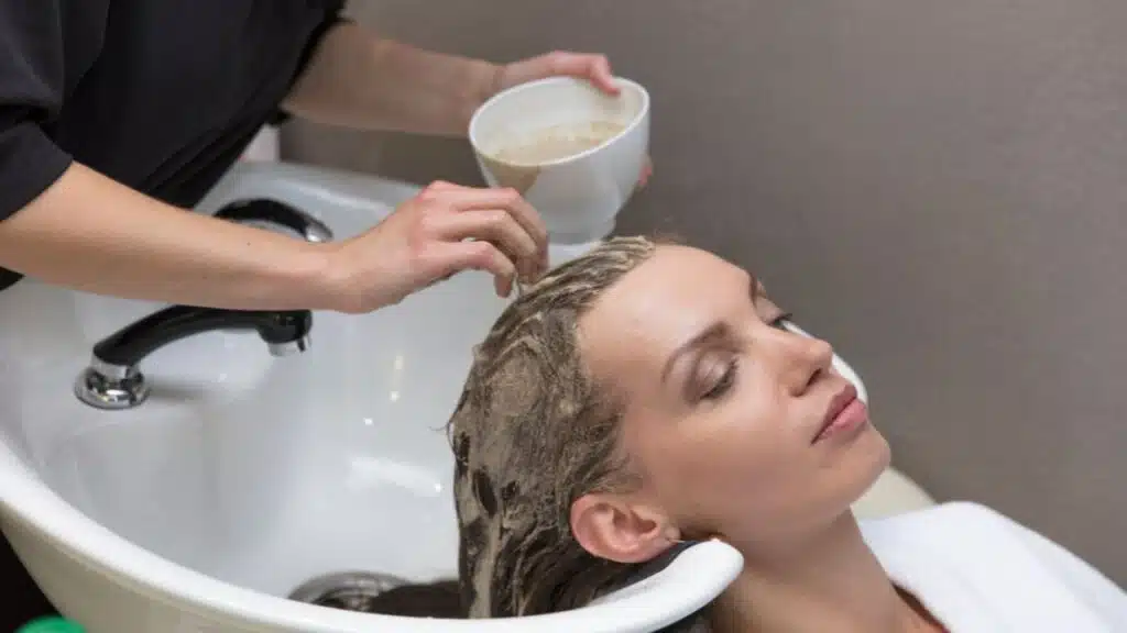 A stylist is applying a hair treatment or shampoo to her scalp from a bowl