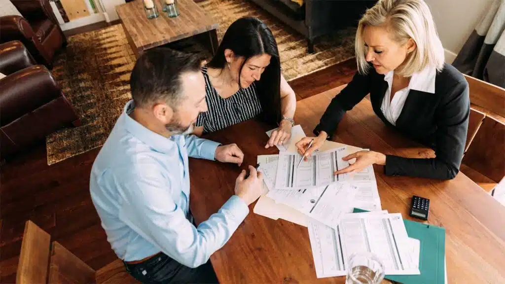 A professional woman is seated at a wooden table, assisting a couple with financial