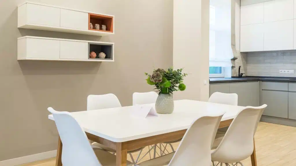Modern dining area with white chairs, a minimalist table, and decorative wall shelves.