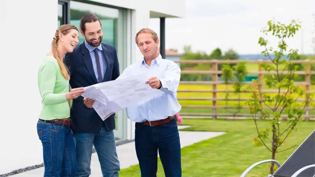 Three people standing outdoors, reviewing a set of blueprints or architectural plans