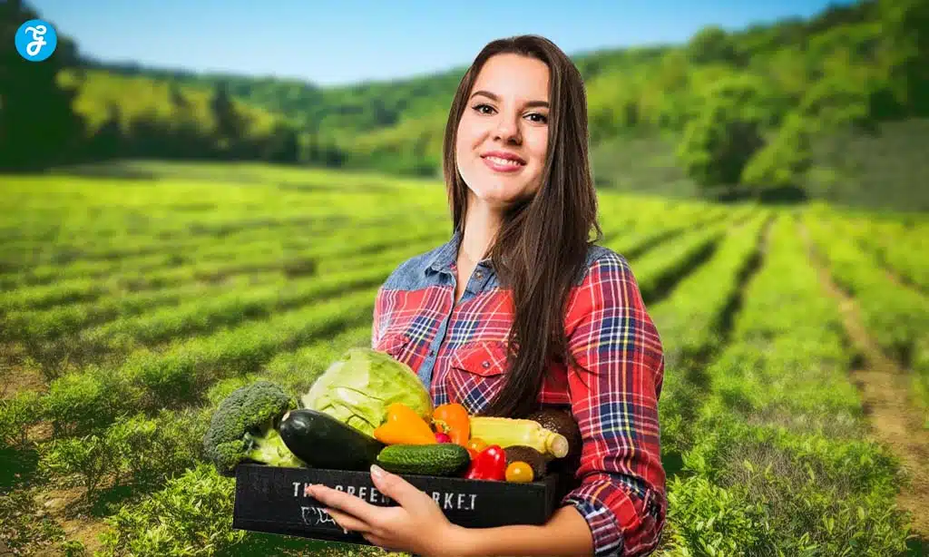 Smiling woman in a plaid shirt holds a box of fresh vegetables in a green farm field