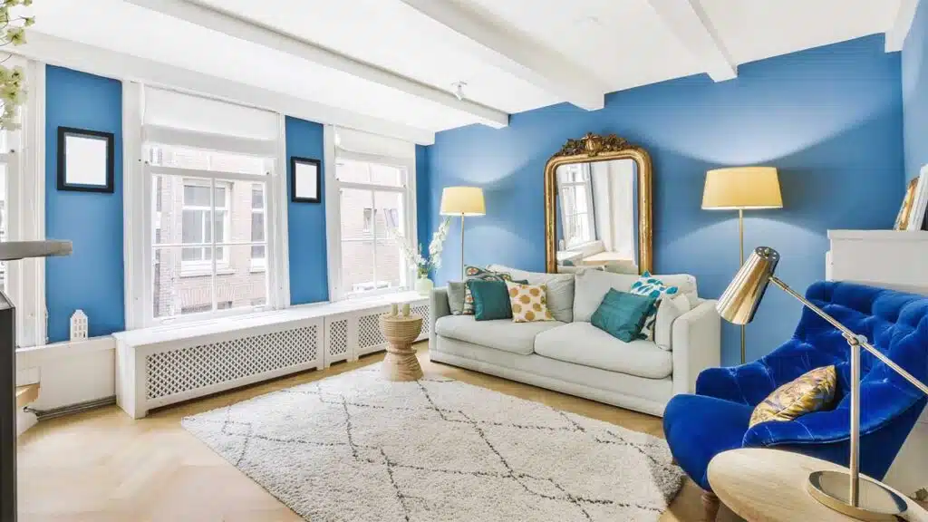 A bright and stylish living room with bold blue walls and large windows letting in plenty of natural light.