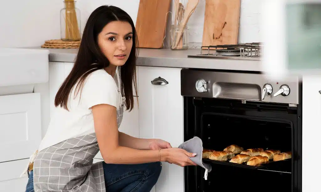 Woman baking fresh pastries in a modern kitchen, taking them out of the oven.